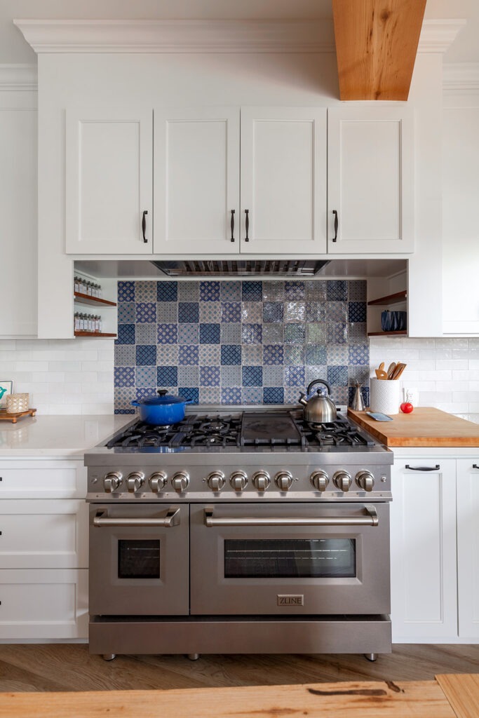 Range detail in kitchen remodel features ZLINE freestanding gas range, quartz countertops, ceramic tile backsplash with blue "patchwork" design.